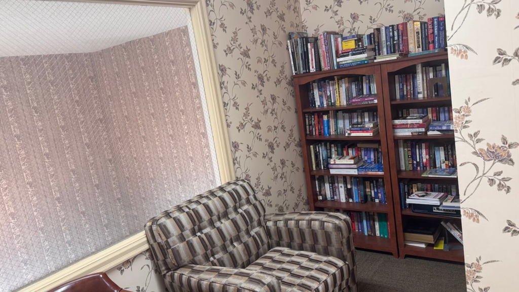 Resident library with comfortable reading chair and bookshelves at Cambridge Place Apartments in Iowa City
